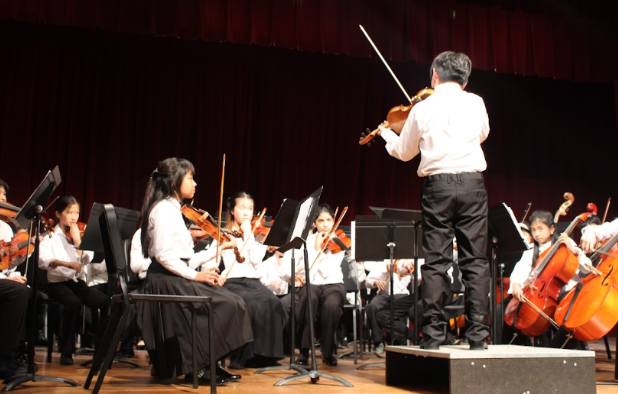 The concert master (Jayden Kim) of the seventh grade orchestra standing on the podium and playing an “A” to help tune the other instruments.
