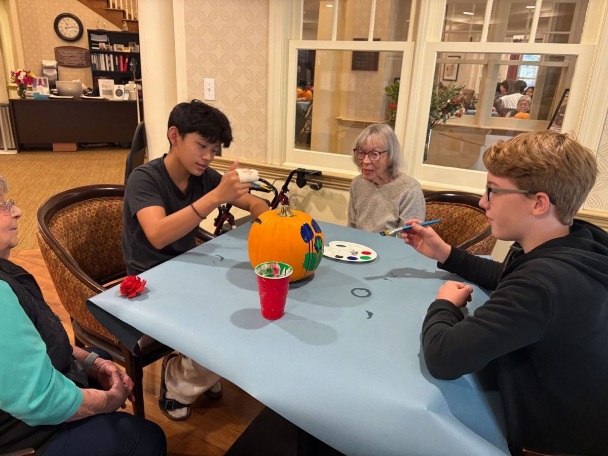 Eighth grade student council members Milo Tseng (left) and Jonas Oleksinski volunteering at Atria Assisted Living and working with residents to paint pumpkins.
