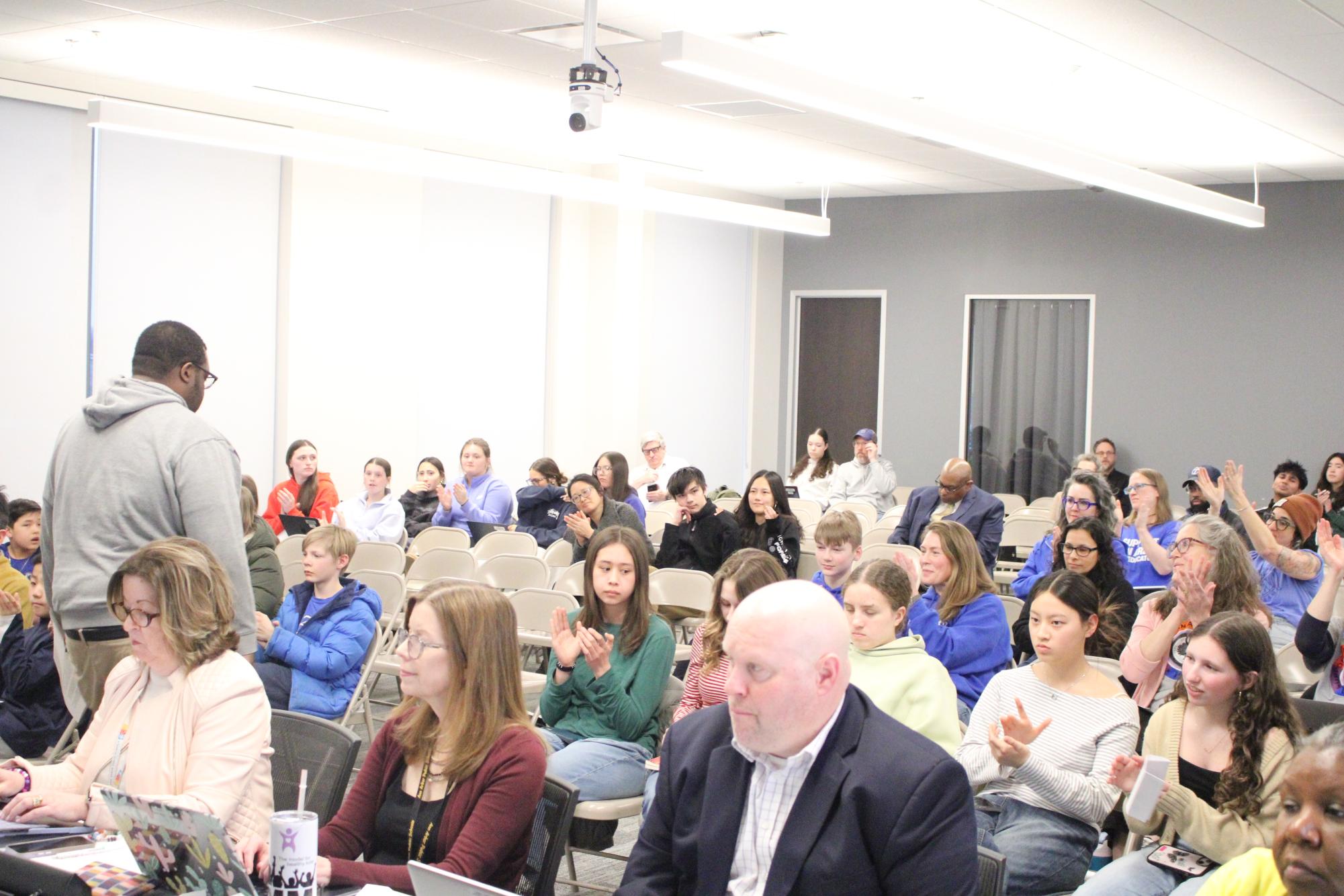 A crowd applauding to the parent (walking down the aisle) that spoke for the AAPS teachers.